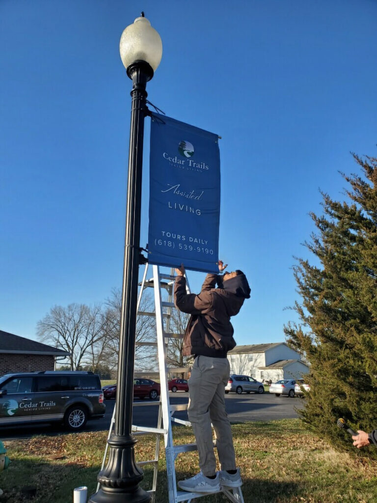 A man hanging a company sign on a lamp post after cleaning it.