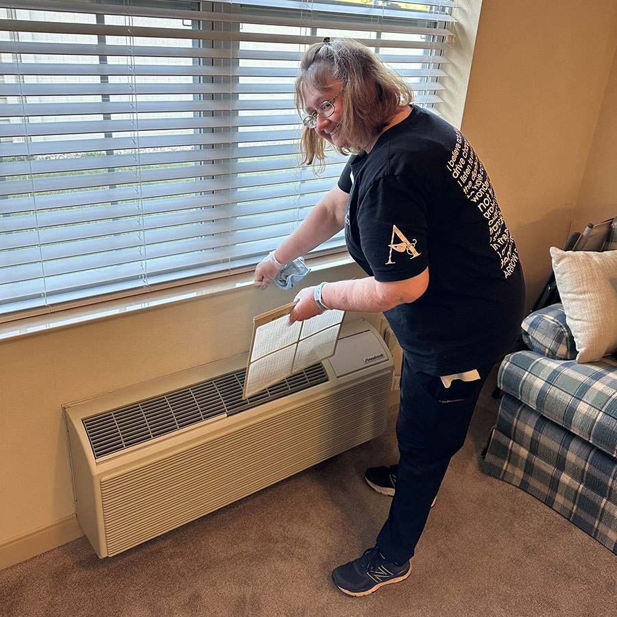 A woman in a black shirt is installing a window air conditioner filter in the room.