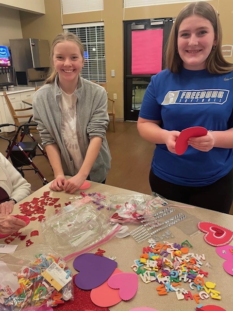 Two young ladies happily crafting valentines with memory care residents in the neighborhood. Love and joy fill the air!