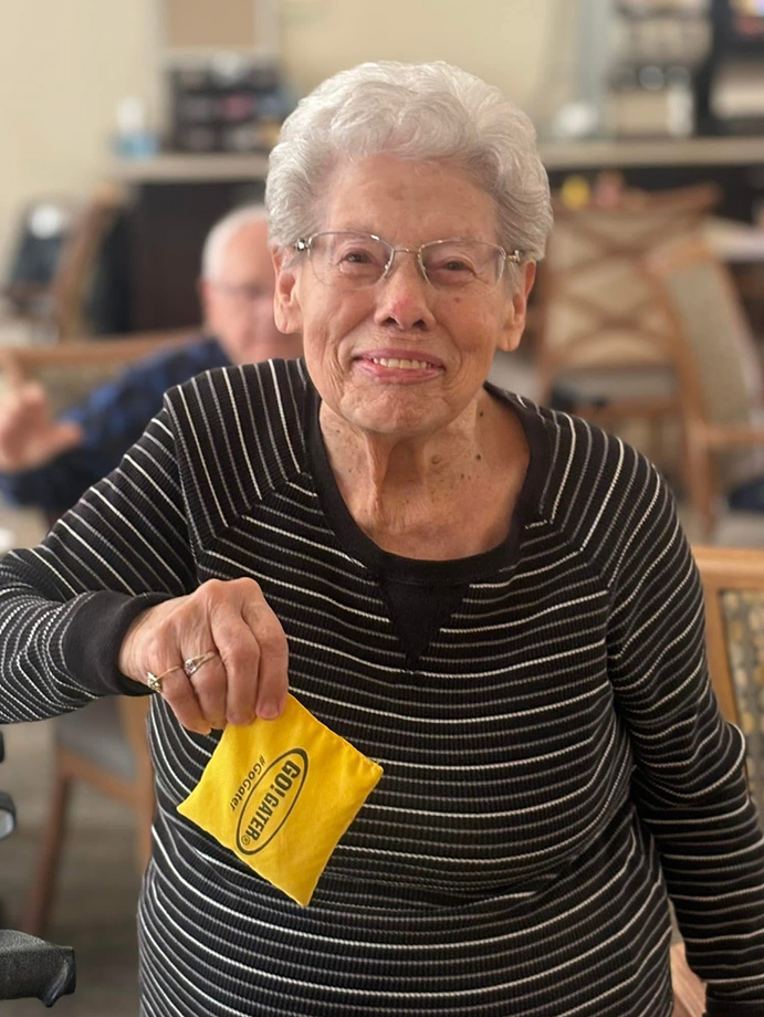 Smiling senior resident holds a yellow beanbag during a lively game at the community, enjoying a fun and interactive event with friends.