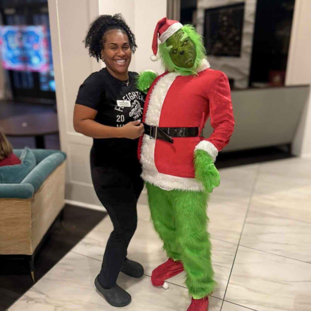 Team member smiles while posing with the Grinch dressed in a Santa suit during a festive holiday celebration at the community.