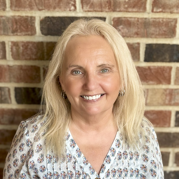 Lori Peterson, Resident Services Director at Cedar Trails Senior Living, smiling in a light blouse with a small paisley pattern in front of a brick wall.