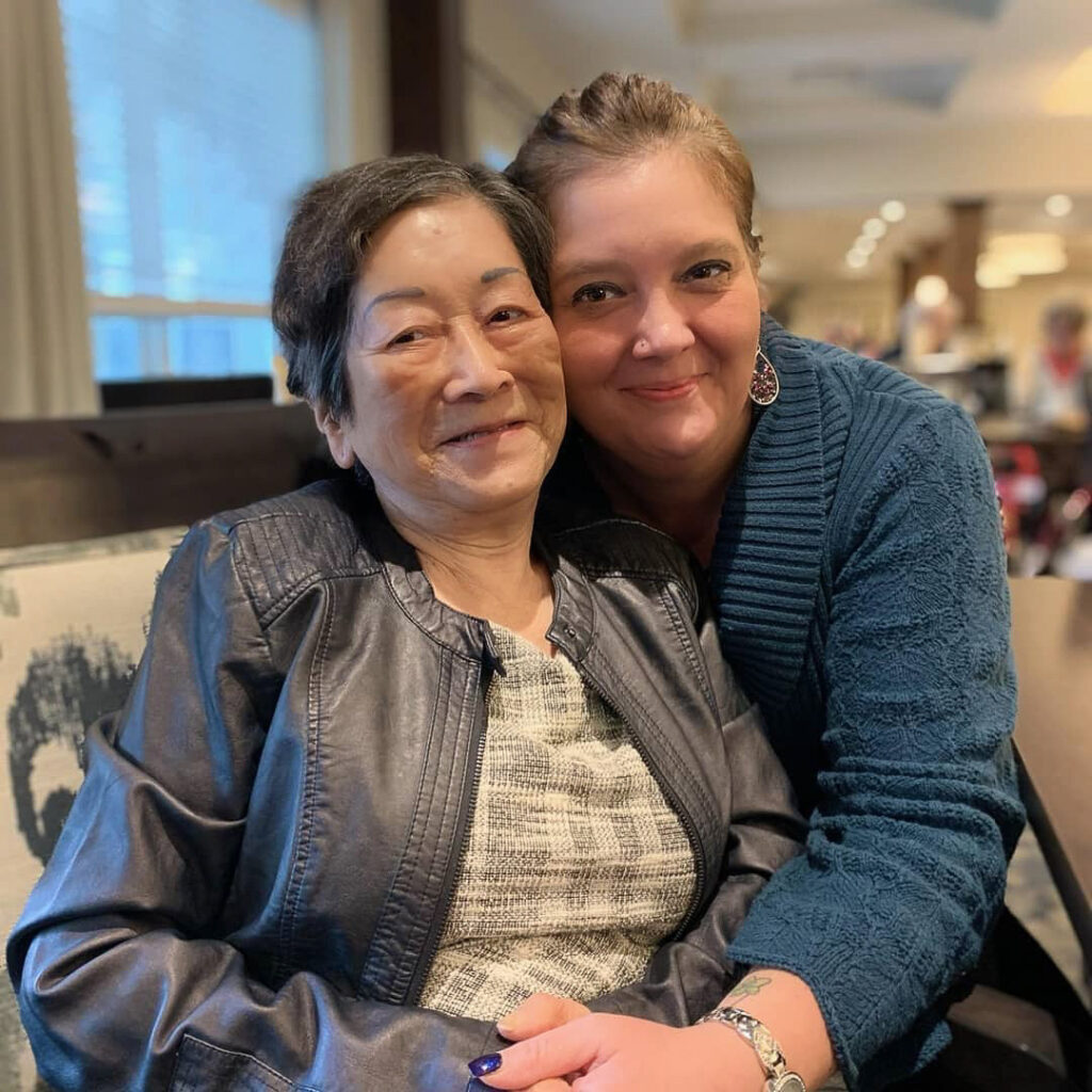 A resident and team member share a close embrace, smiling warmly together and highlighting connection and care within the senior living community.