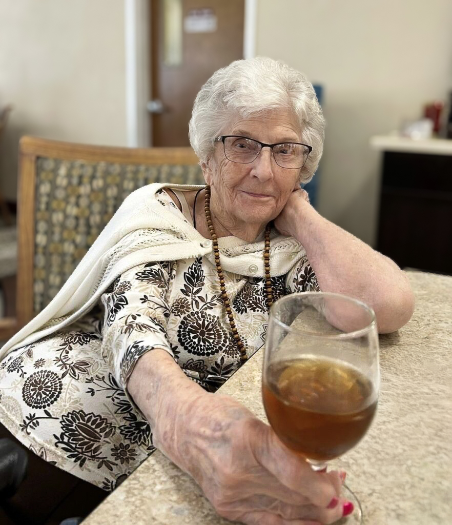 A senior woman relaxes, smiling with a wine glass full of cold drink in one hand.