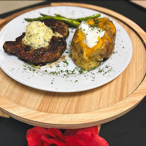 A chef-prepared Valentines dinner of seared steak with herb butter, loaded baked potato, and fresh asparagus.