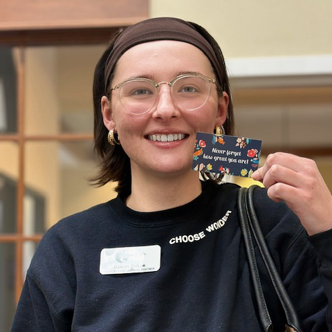 A woman on the Cedar Trails team smiles brightly, holding a card that reads "never forget how great you are".