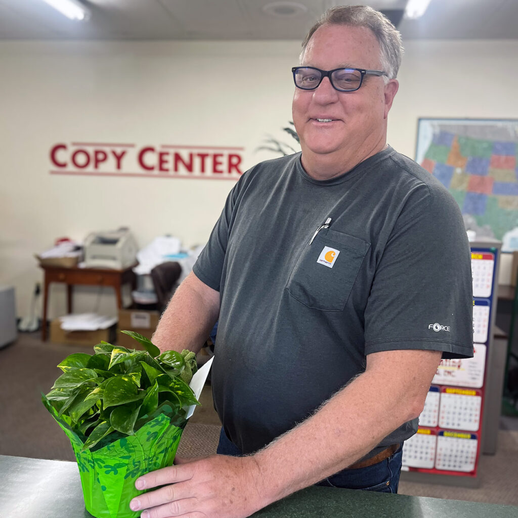 A local business owner smiles with a plant gifted by Cedar Trails Senior Living.