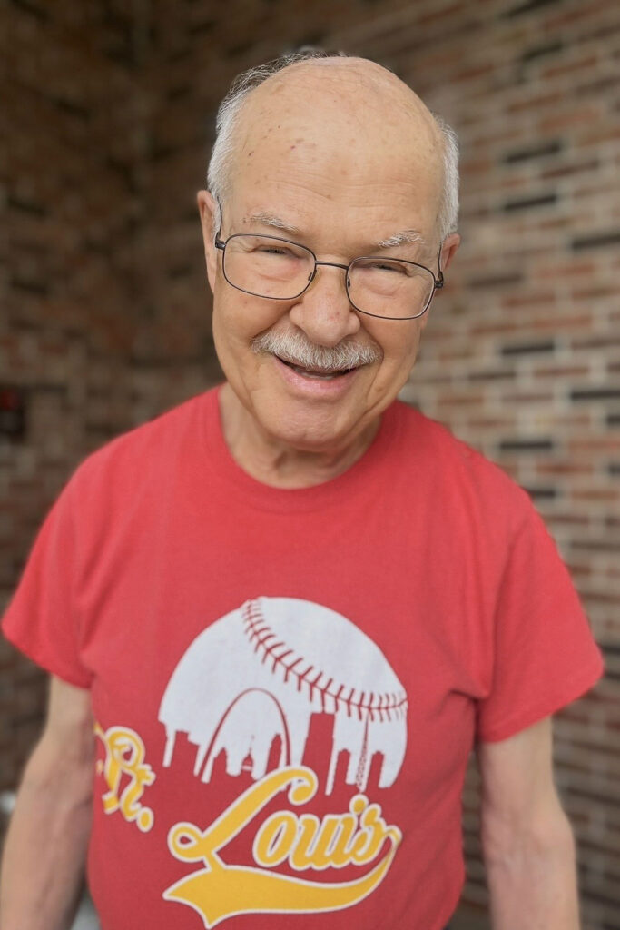 A senior man wearing a baseball tshirt smiles at Cedar Trails Senior Living.